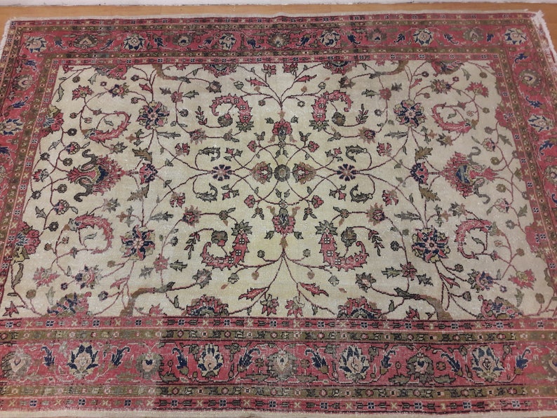 May include: A vintage cream-colored rug with a floral pattern in shades of pink, green, and blue. The rug has a border with a repeating pattern of pink, green, and blue.