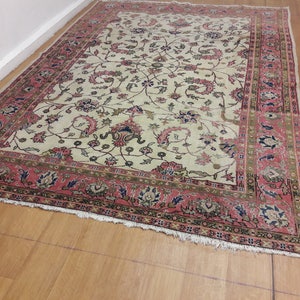 May include: A vintage cream-colored rug with a floral pattern in shades of pink, green, and blue. The rug has a red border with a geometric design.