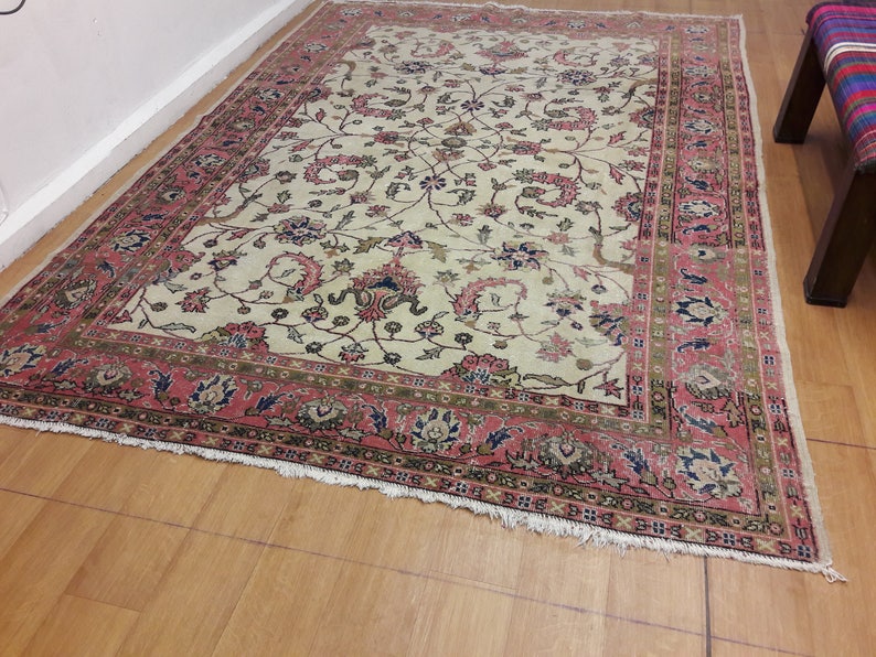 May include: A vintage cream-colored rug with a floral pattern in shades of pink, green, and blue. The rug has a red border with a geometric design.