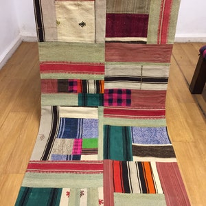 Può includere: Un tappeto patchwork con una varietà di colori e motivi, tra cui rosso, verde, blu e bianco. Il tappeto è realizzato in tessuto tessuto e ha un aspetto rustico e fatto a mano.