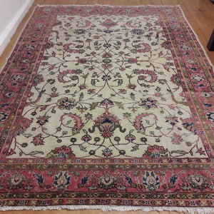May include: A vintage cream-colored rug with a floral pattern in shades of pink, green, and blue. The rug has a detailed border with a repeating pattern.