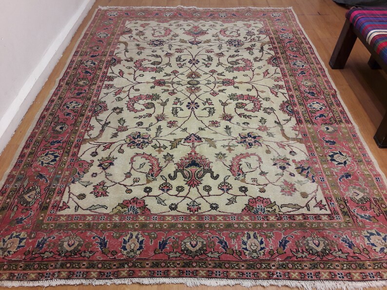 May include: A vintage cream-colored rug with a floral pattern in shades of pink, green, and blue. The rug has a detailed border with a repeating pattern.