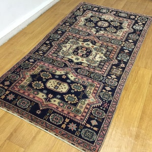 May include: A traditional Persian rug with a navy blue background and intricate patterns in shades of pink, cream, and green. The rug features a repeating geometric design with a central medallion.