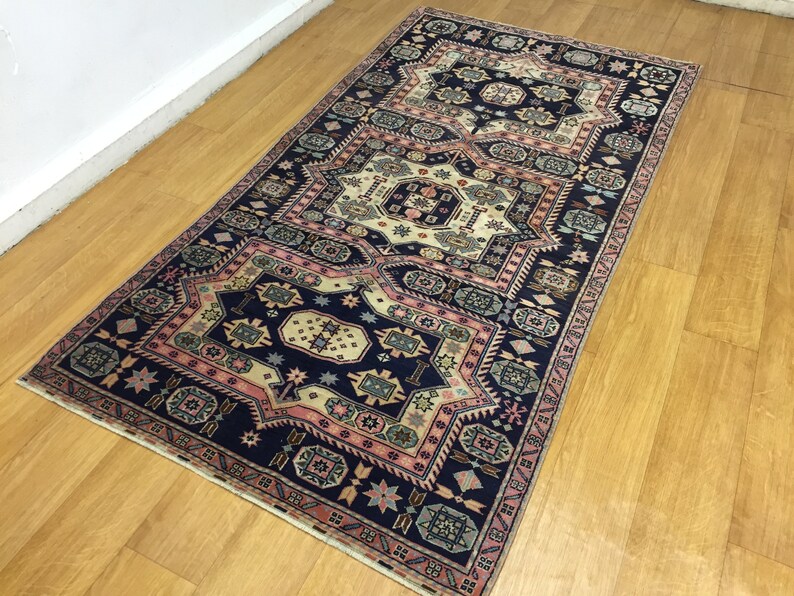 May include: A traditional Persian rug with a navy blue background and intricate patterns in shades of pink, cream, and green. The rug features a repeating geometric design with a central medallion.