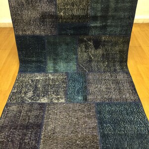 May include: A patchwork rug made from different shades of blue denim fabric. The rug is made up of squares of fabric sewn together to create a unique and interesting design.