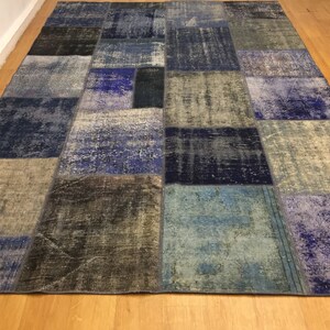 Könnte beinhalten: Ein Patchwork-Teppich mit verschiedenen blauen, grauen und schwarzen Quadraten. Der Teppich ist aus recycelten Materialien hergestellt und hat einen Used-Look.