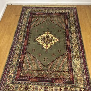 May include: A traditional rug with a green center and intricate patterns in shades of red, blue, and beige. The rug has a fringed edge.