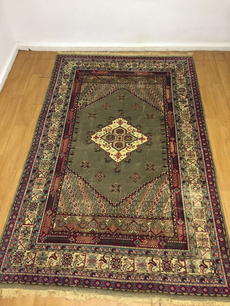 May include: A traditional rug with a green center and intricate patterns in shades of red, blue, and beige. The rug has a fringed edge.
