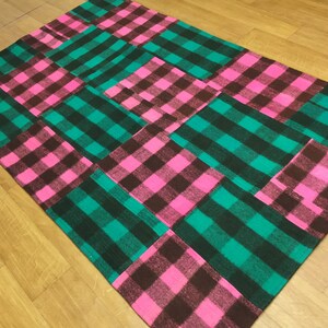 Könnte beinhalten: Ein Patchwork-Teppich mit einem karierten Muster in den Farben Rosa, Grün und Braun.