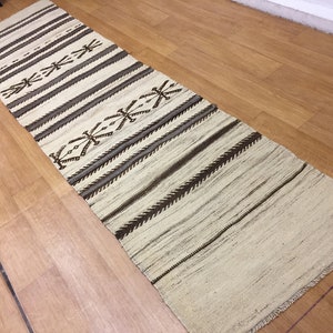 May include: A white and brown striped runner rug with a geometric pattern. The rug has a fringe border.