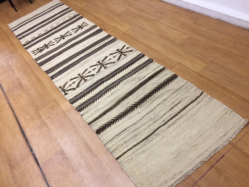 May include: A white and brown striped runner rug with a geometric pattern. The rug has a fringe border.