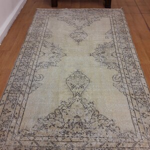 May include: A vintage rug with a light beige background and a dark brown floral pattern. The rug has a distressed look and is perfect for adding a touch of rustic charm to any room.