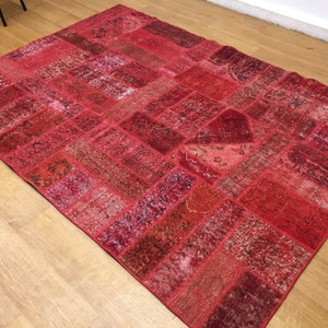 May include: A red patchwork rug with a variety of patterns and textures. The rug is made up of many different pieces of fabric that have been sewn together.