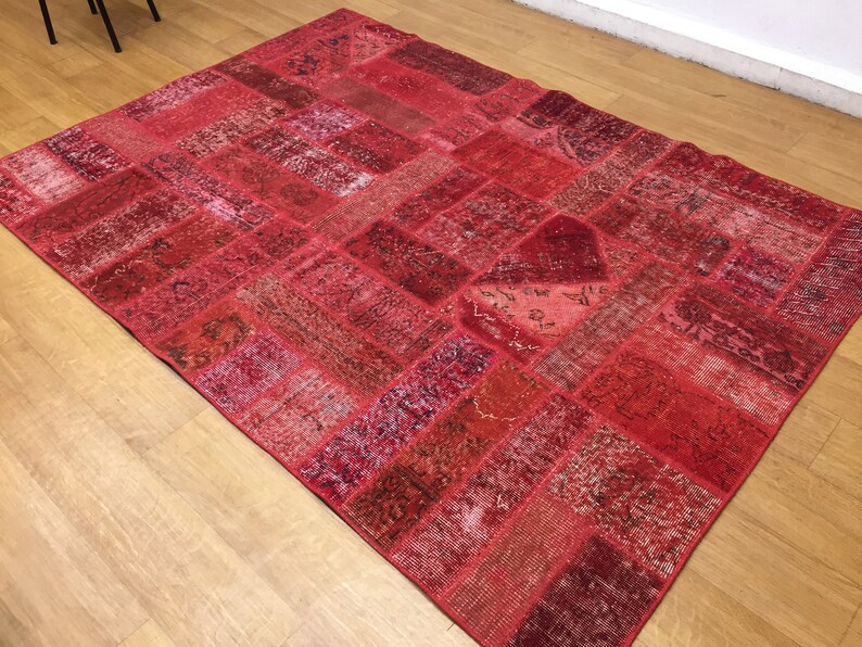 May include: A red patchwork rug with a variety of patterns and textures. The rug is made up of many different pieces of fabric that have been sewn together.