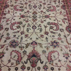May include: A vintage rug with a cream background and intricate floral patterns in shades of pink, red, and black. The rug has a border with a repeating pattern.