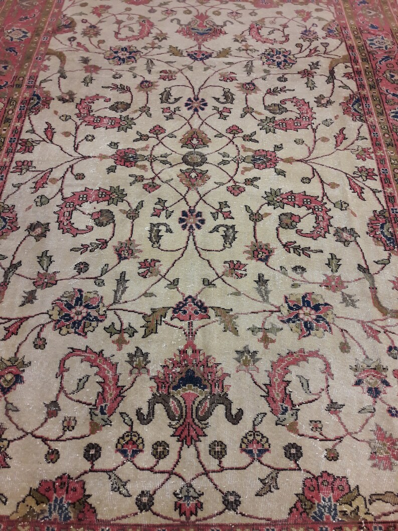 May include: A vintage rug with a cream background and intricate floral patterns in shades of pink, red, and black. The rug has a border with a repeating pattern.
