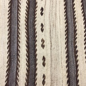 May include: Close-up of a woven rug with a white background and brown and gray stripes. The stripes are made of a zig-zag pattern.