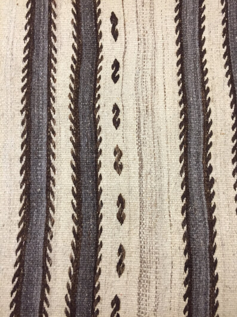 May include: Close-up of a woven rug with a white background and brown and gray stripes. The stripes are made of a zig-zag pattern.