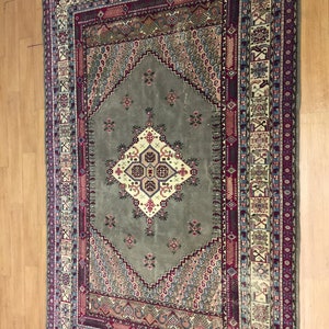 May include: A vintage rug with a green center and intricate patterns in shades of red, blue, and cream. The rug has a fringed edge and is made of wool.