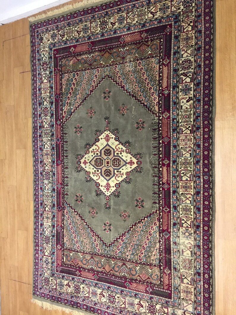 May include: A vintage rug with a green center and intricate patterns in shades of red, blue, and cream. The rug has a fringed edge and is made of wool.