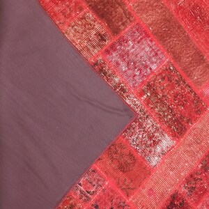 May include: A red and pink patchwork rug with a dark brown backing. The rug is made of different pieces of fabric sewn together.