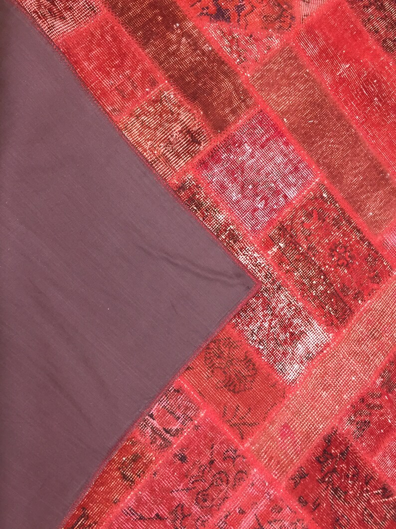 May include: A red and pink patchwork rug with a dark brown backing. The rug is made of different pieces of fabric sewn together.
