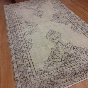 May include: A vintage cream-colored rug with a black and white geometric pattern. The rug has a faded look and is made of a soft, woven material.
