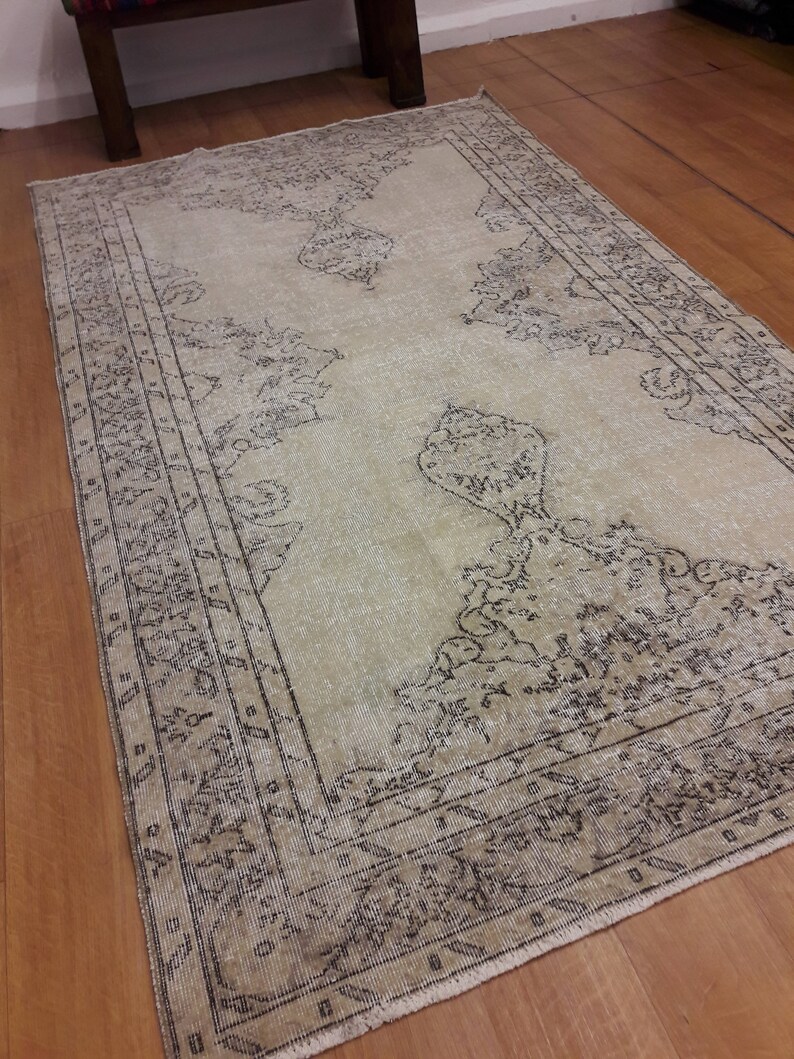 May include: A vintage cream-colored rug with a black and white geometric pattern. The rug has a faded look and is made of a soft, woven material.