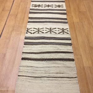 May include: A long, narrow, white rug with brown geometric patterns. The rug has a fringe on the bottom edge.
