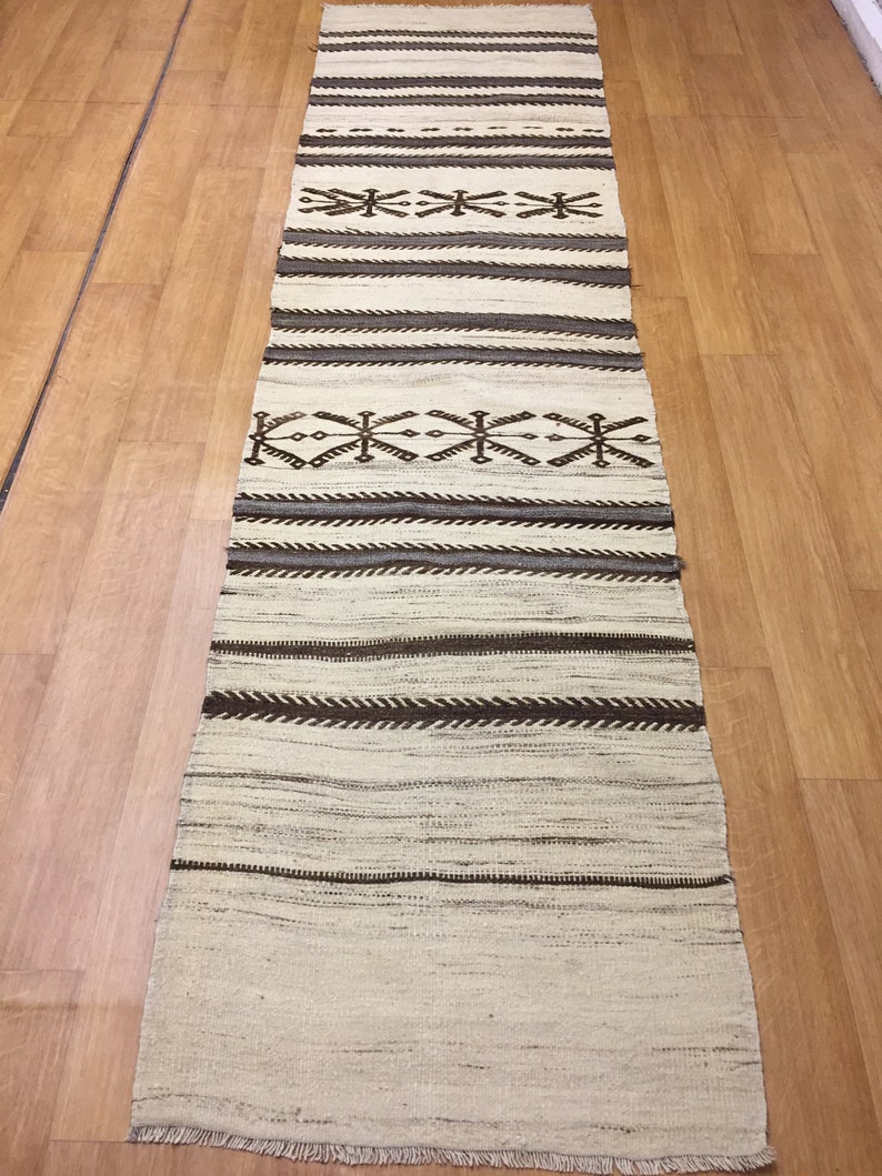 May include: A long, narrow, white rug with brown geometric patterns. The rug has a fringe on the bottom edge.