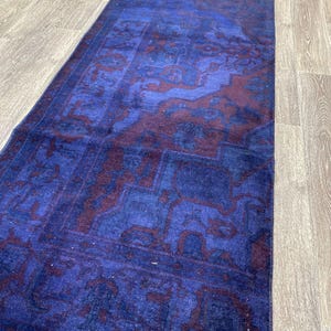 Pu&ograve; includere: Un tappeto vintage blu e bordeaux con un designo persiano tradizionale. Il tappeto ha un aspetto sbiadito e usurato ed &egrave; fatto di lana.