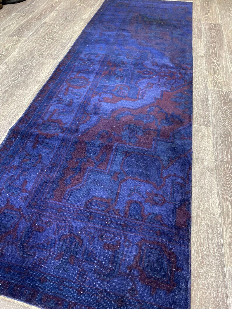 Pu&ograve; includere: Un tappeto vintage blu e bordeaux con un designo persiano tradizionale. Il tappeto ha un aspetto sbiadito e usurato ed &egrave; fatto di lana.