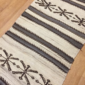 May include: A white and brown woven rug with a geometric pattern. The rug has a striped design with a repeating pattern of brown and white.