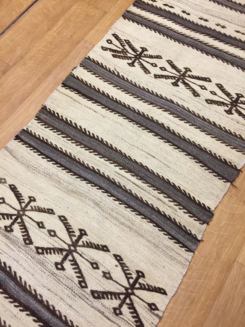 May include: A white and brown woven rug with a geometric pattern. The rug has a striped design with a repeating pattern of brown and white.
