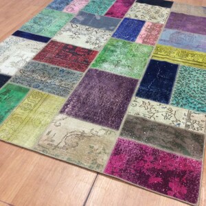 Könnte beinhalten: Ein bunter Patchwork-Teppich mit verschiedenen Grüntönen, Blau, Lila, Rot und Gelb. Der Teppich besteht aus verschiedenen Stoffen und Texturen und erzeugt so ein einzigartiges und vielseitiges Design.