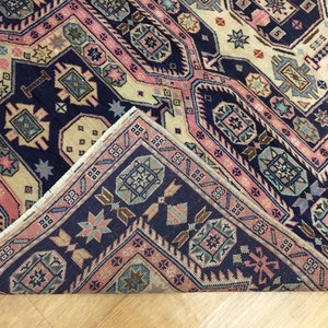May include: A close-up of the corner of a rug with a navy blue background and a geometric pattern in shades of pink, beige, and blue.