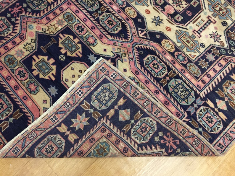 May include: A close-up of the corner of a rug with a navy blue background and a geometric pattern in shades of pink, beige, and blue.