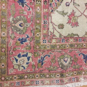 May include: Close-up of a pink and cream rug with a floral pattern. The rug has a fringe border and is made of wool.