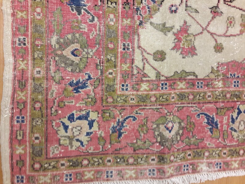 May include: Close-up of a pink and cream rug with a floral pattern. The rug has a fringe border and is made of wool.