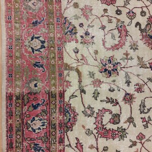 May include: A vintage rug with a cream background and a floral pattern in shades of pink, red, blue, and green. The rug has a border with a geometric pattern in shades of red, green, and brown.