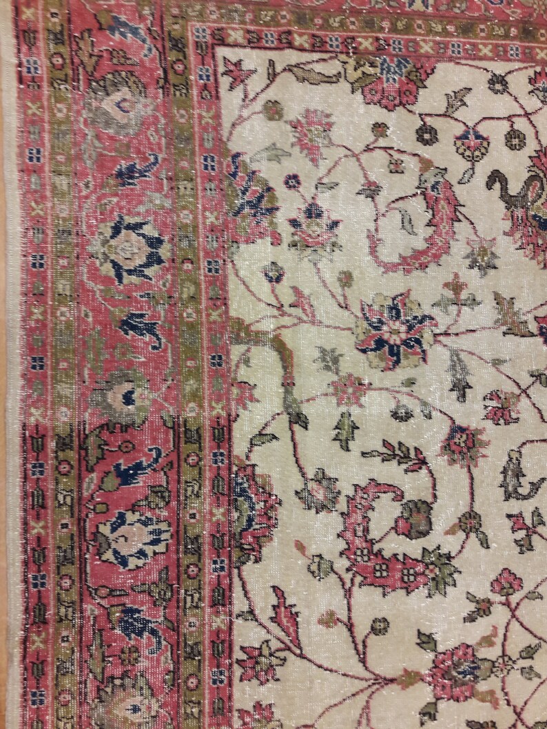 May include: A vintage rug with a cream background and a floral pattern in shades of pink, red, blue, and green. The rug has a border with a geometric pattern in shades of red, green, and brown.