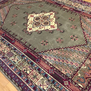 May include: A vintage rug with a geometric pattern in shades of red, blue, and beige. The rug has a central medallion with a floral design.