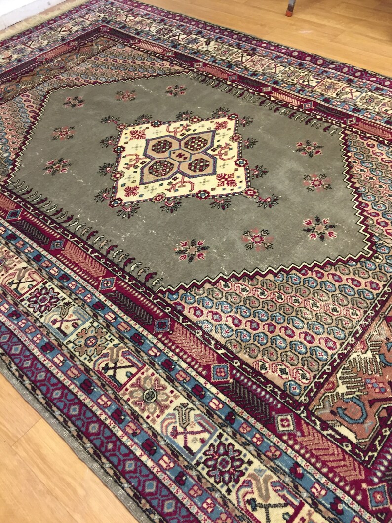 May include: A vintage rug with a geometric pattern in shades of red, blue, and beige. The rug has a central medallion with a floral design.