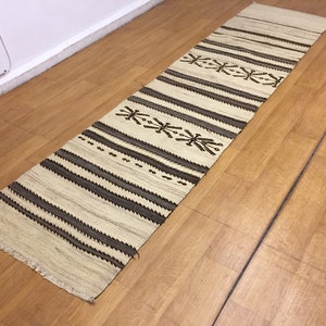 May include: A white and brown striped runner rug with a geometric pattern. The rug has a fringe border.