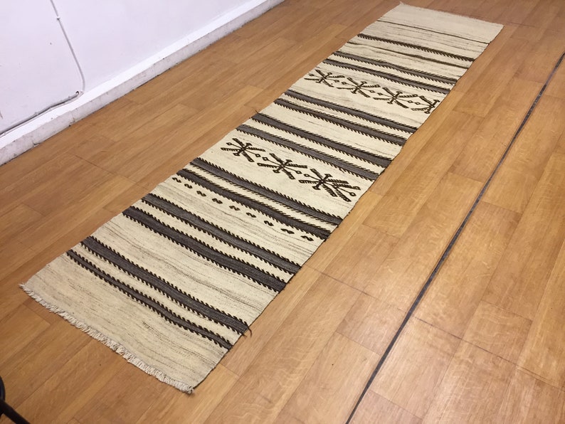 May include: A white and brown striped runner rug with a geometric pattern. The rug has a fringe border.