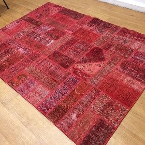 May include: A red patchwork rug with a variety of patterns and textures. The rug is made from recycled materials and has a distressed look.