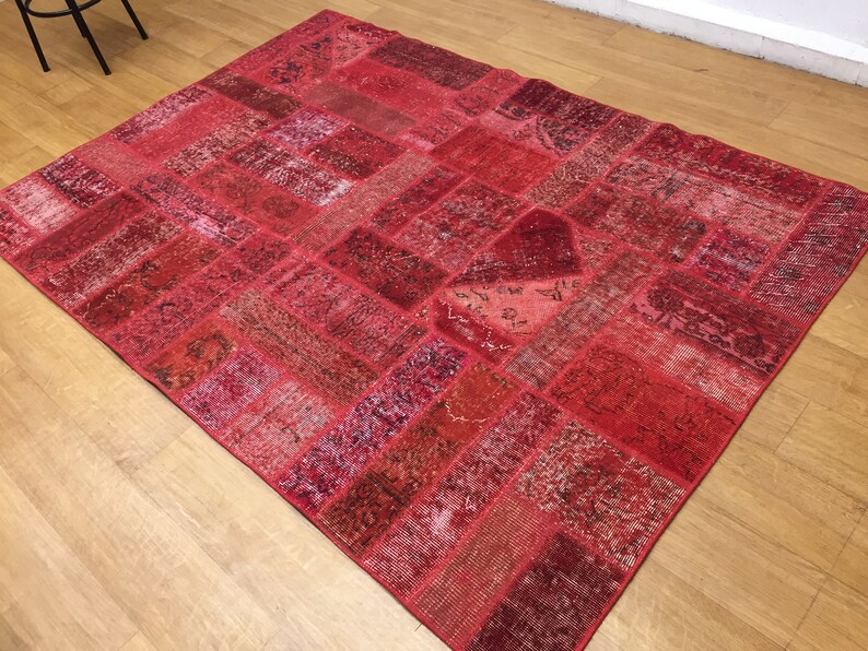 May include: A red patchwork rug with a variety of patterns and textures. The rug is made from recycled materials and has a distressed look.