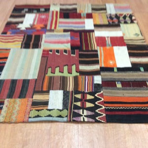 Puede incluir: Una alfombra de retazos con una variedad de parches rectangulares y cuadrados en varios colores y patrones. La alfombra presenta rayas, zigzags y colores lisos como el rojo, naranja, negro y beige. La alfombra está colocada sobre un suelo de madera.