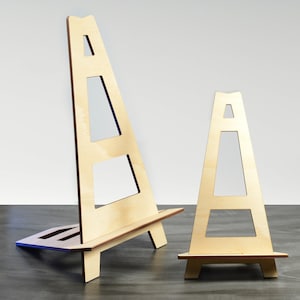 May include: Two wooden easels, one large and one small, are made of light brown wood. The easels are standing on a dark grey surface.