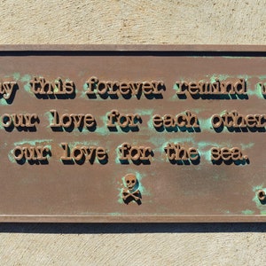 May include: A rectangular bronze plaque with embossed text that reads "May this forever remind us of our love for each other & our love for the sea." A skull and crossbones symbol is below the text.